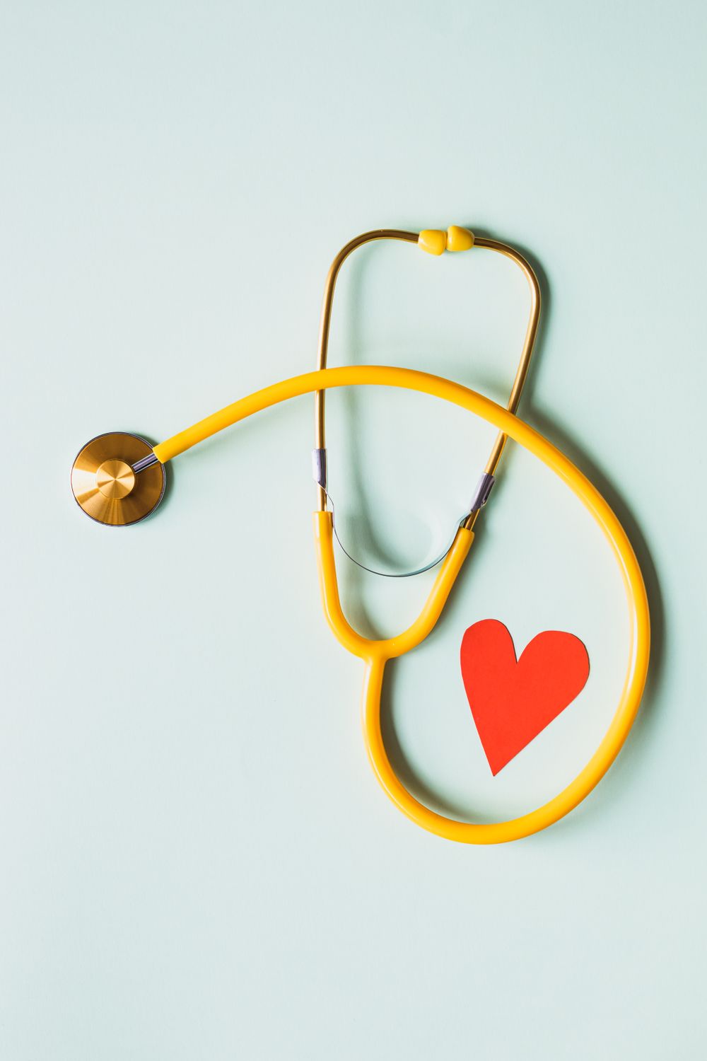 A yellow stethoscope curved around a small red paper heart