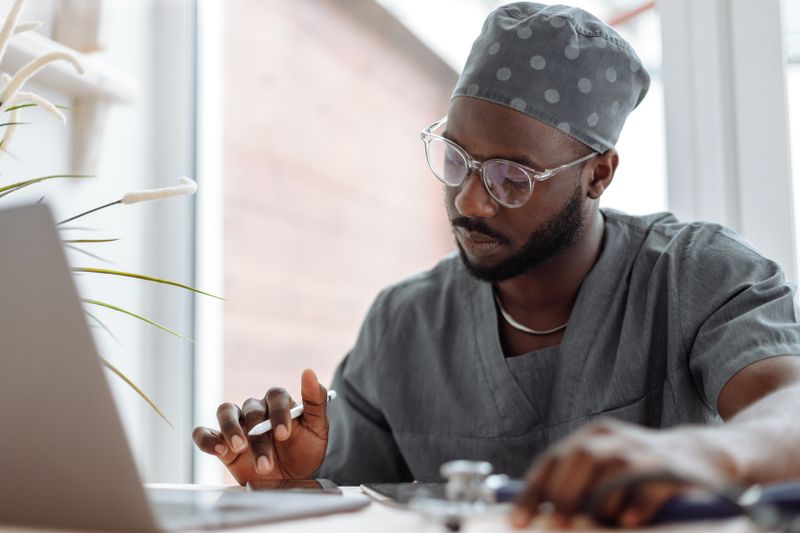 Andre Cole in clinical scrubs at a laptop