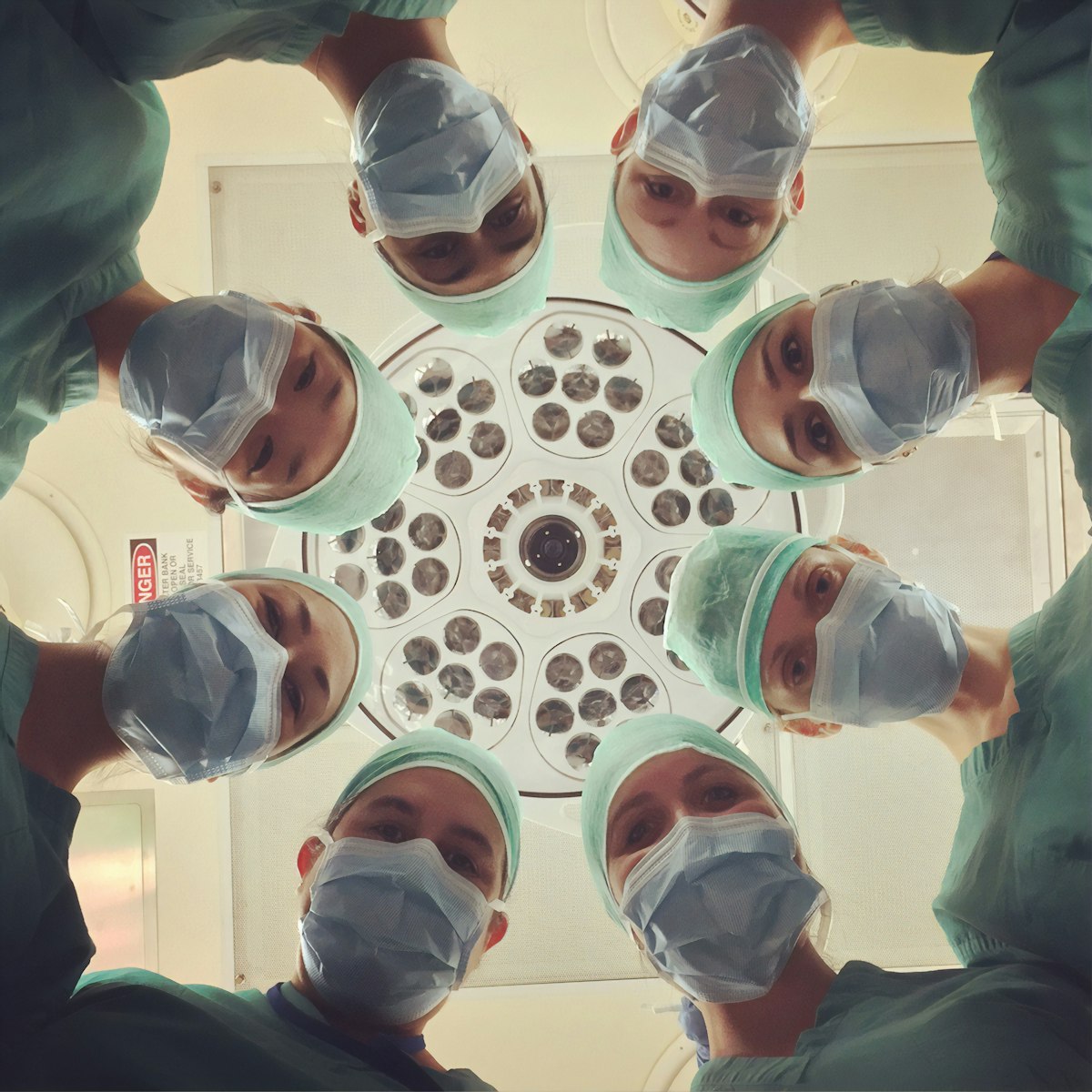 A clinical team in masks gathered under a surgical light